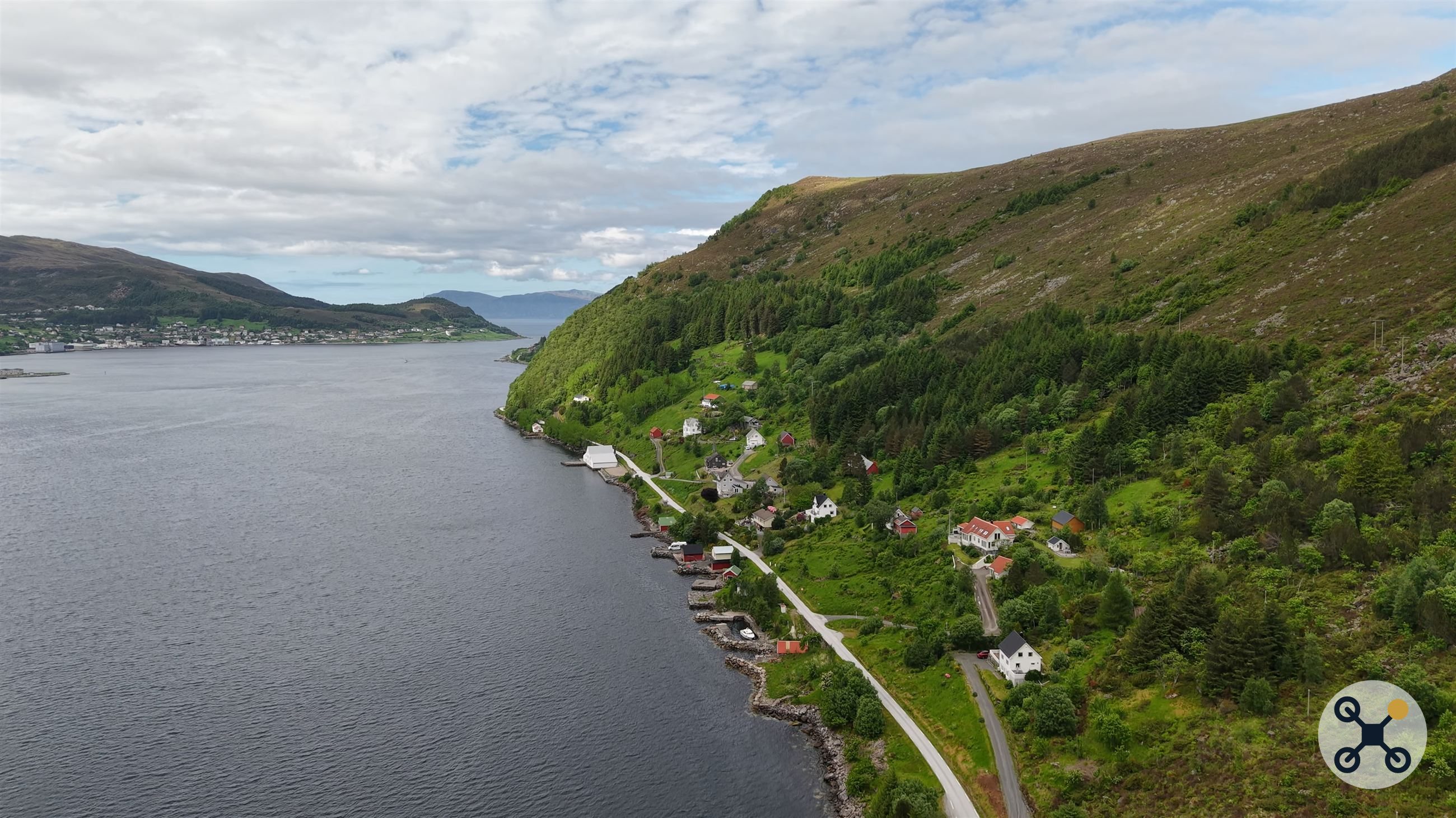 Spredt bebyggelse langs fjordkanten, med fjell og skyer i bakgrunnen.