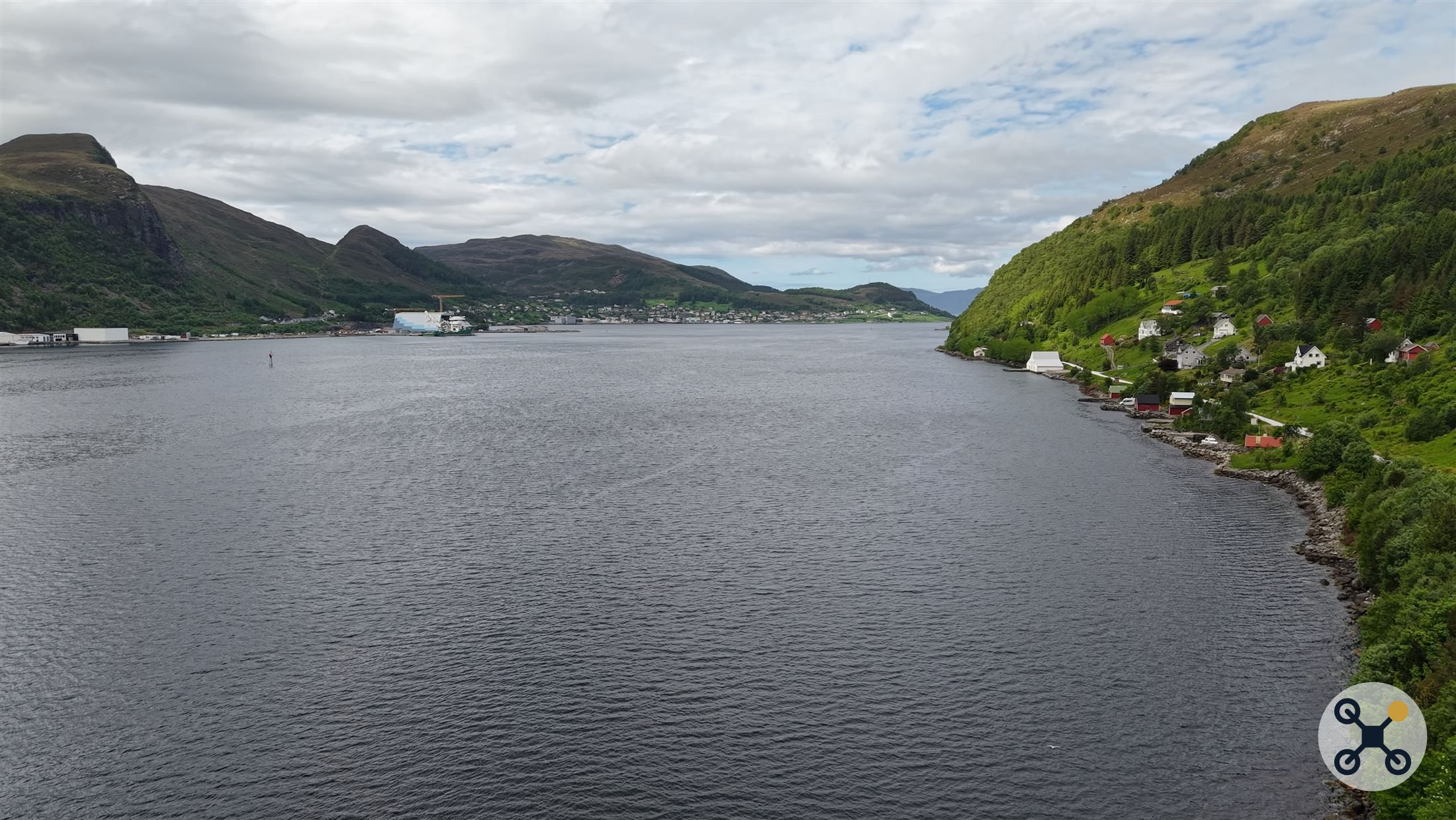 Utsikt over fjorden mot havn og tettsted, med grønne fjellsider på hver side.