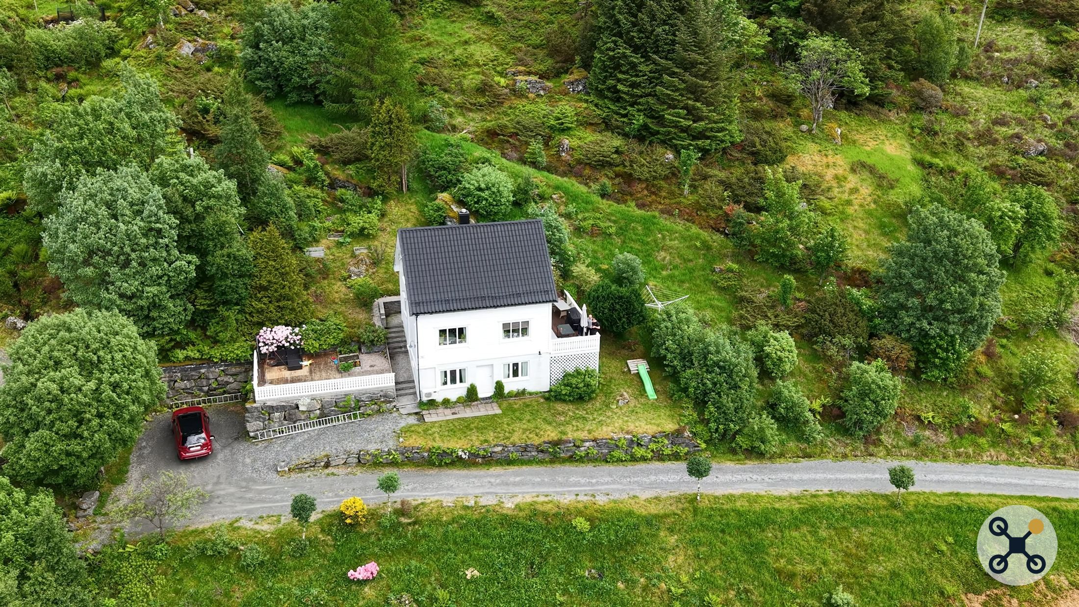 Skråfoto av hvit enebolig omgitt av hage og skog.