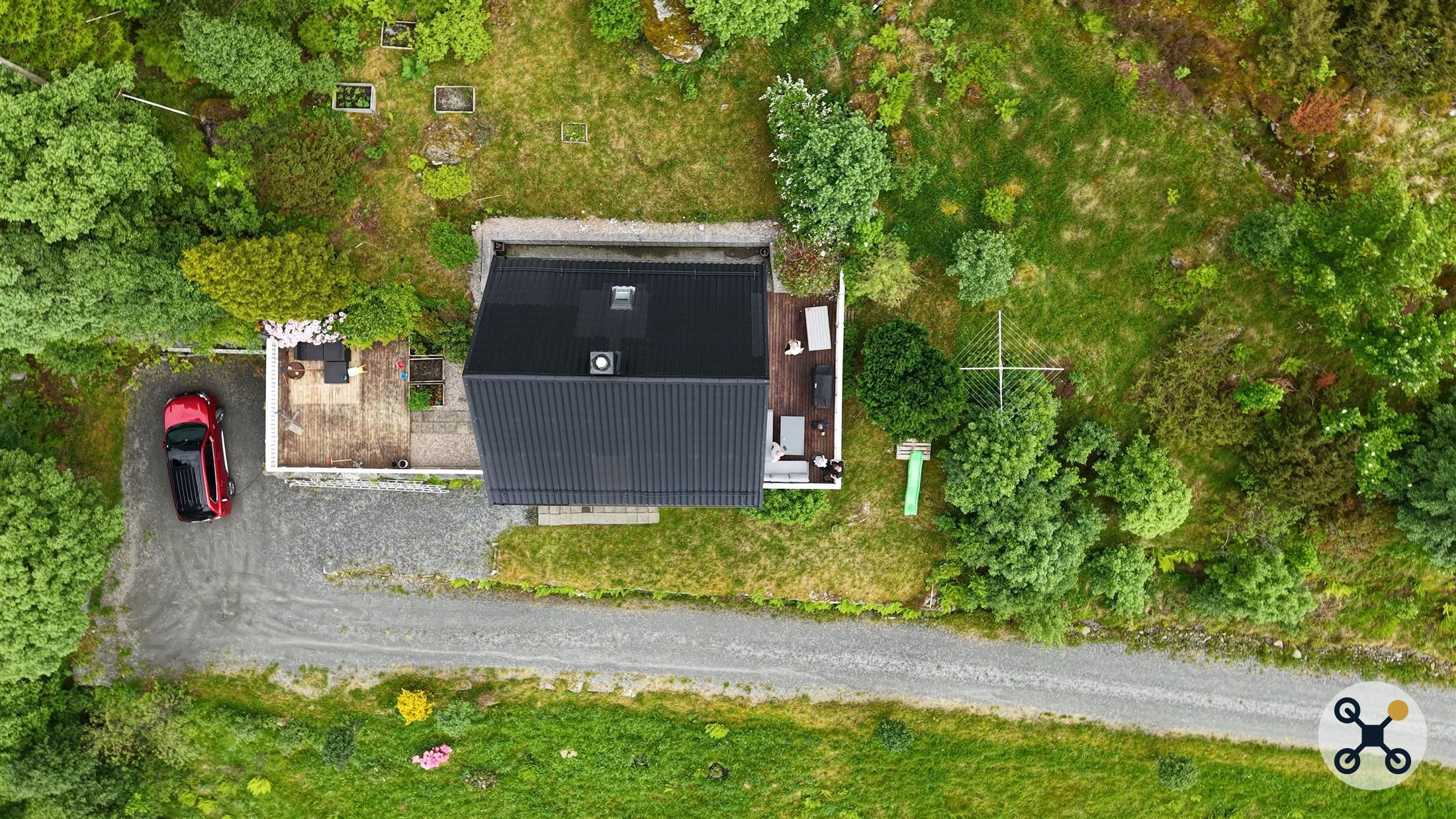 Rett-ned-foto av enebolig med sort tak, tatt med drone.