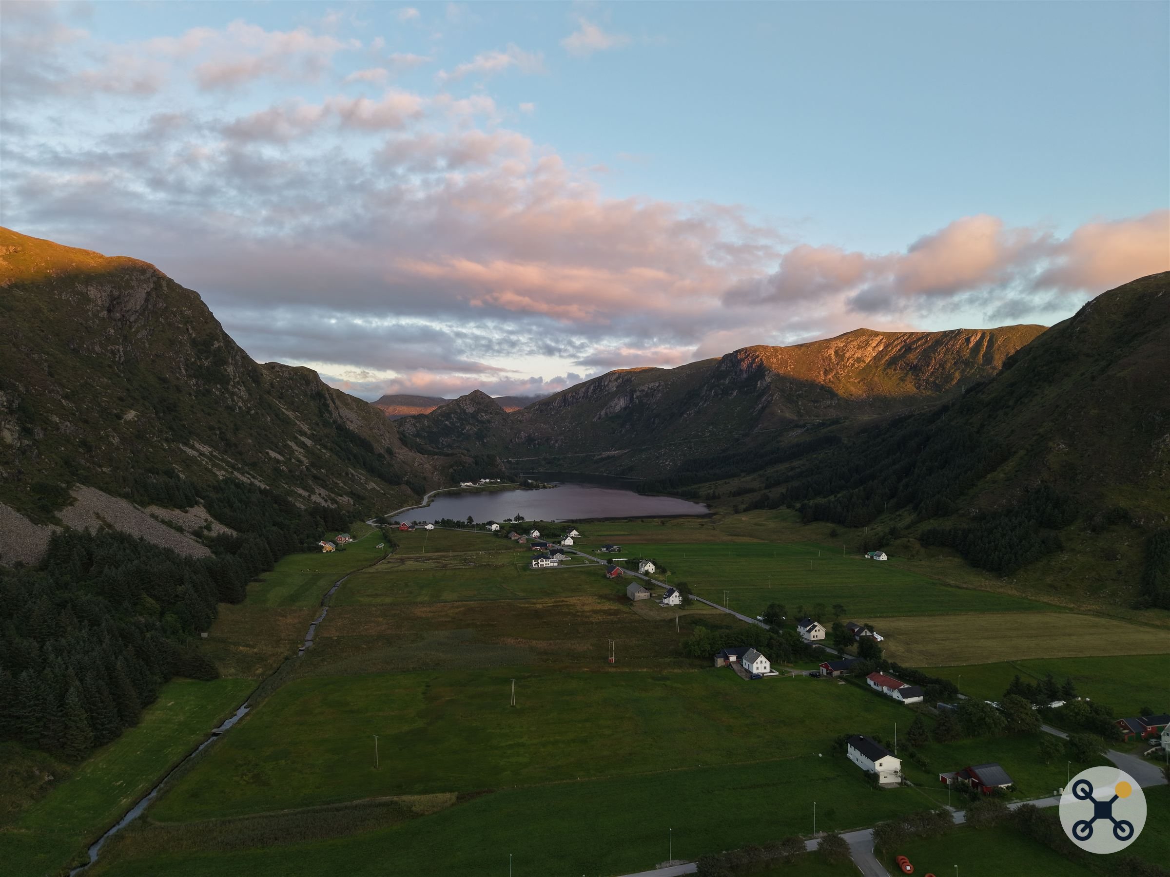 Dalen ved Refvik sett fra drone, med innsjø, spredt bebyggelse og fjell i kveldslys.